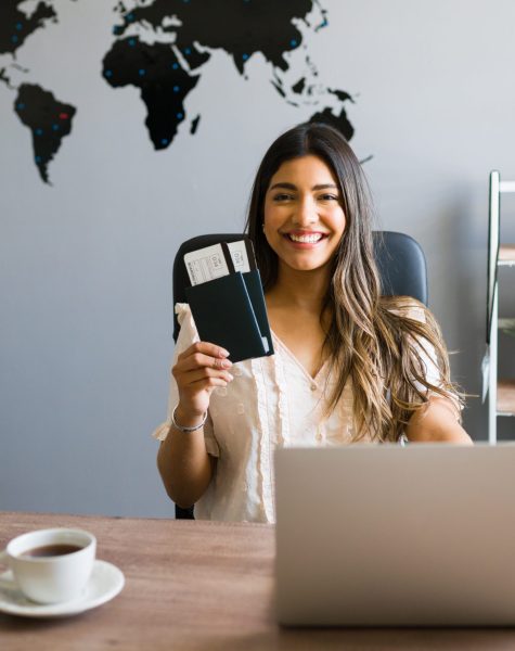 I am here to help you with your booking and travel questions. Female sales agent holding plane tickets while smiling and making eye contact at the travel agency